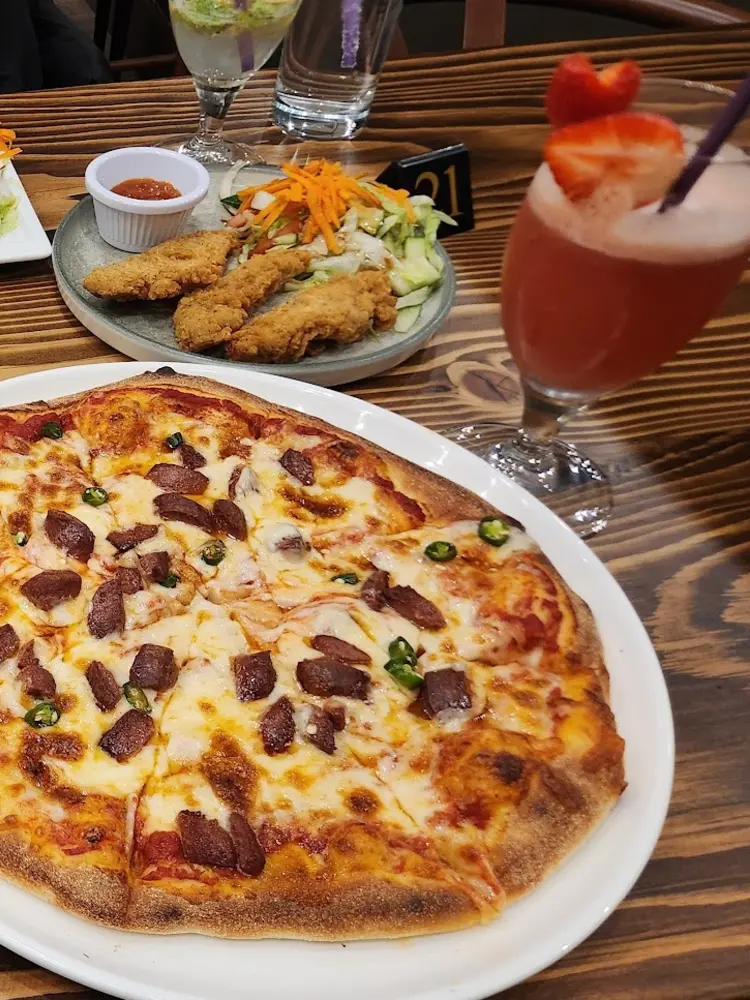 Table spread with a sucuk pizza, hummus with flatbread, borek rolls and a strawberry drink