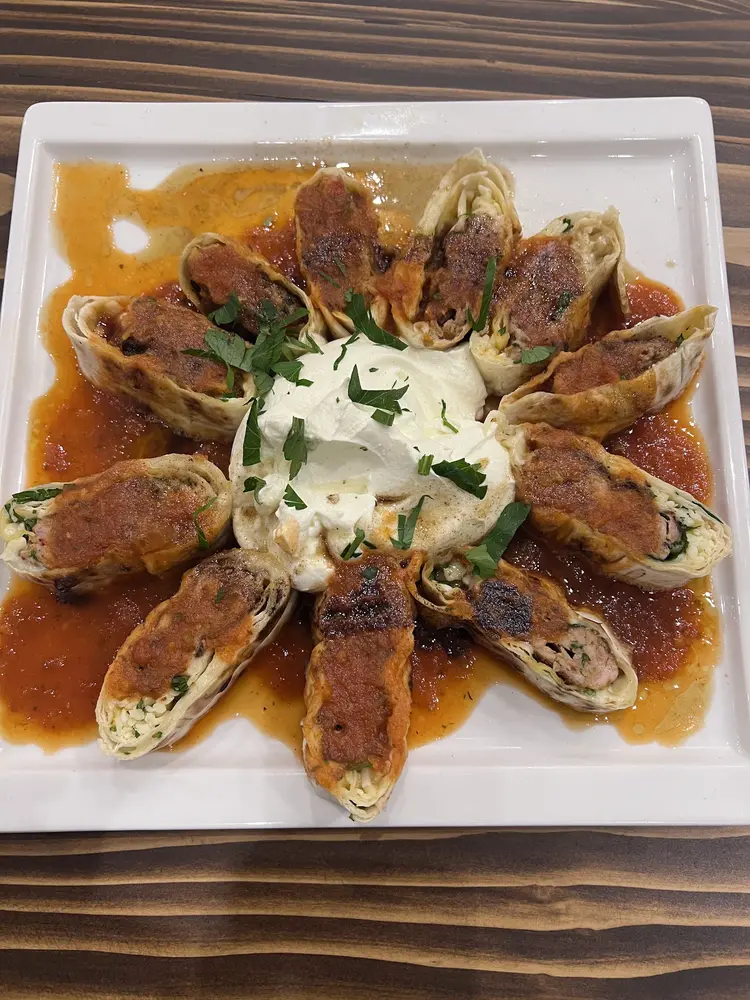 Sliced kebab wrapped in flatbread, arranged around a mound of yoghurt with tomato sauce