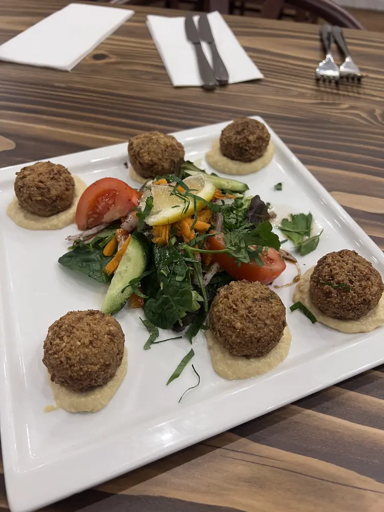Six falafel balls set on hummus around a dressed salad on a white square plate